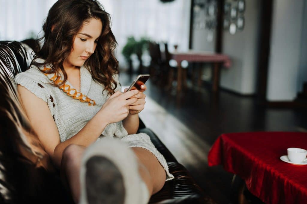 Happy young woman looking at mobile phone in bed