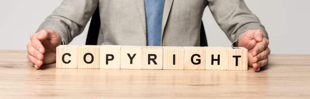 partial view of businessman sitting at desk near wooden cubes with word copyright isolated on grey,